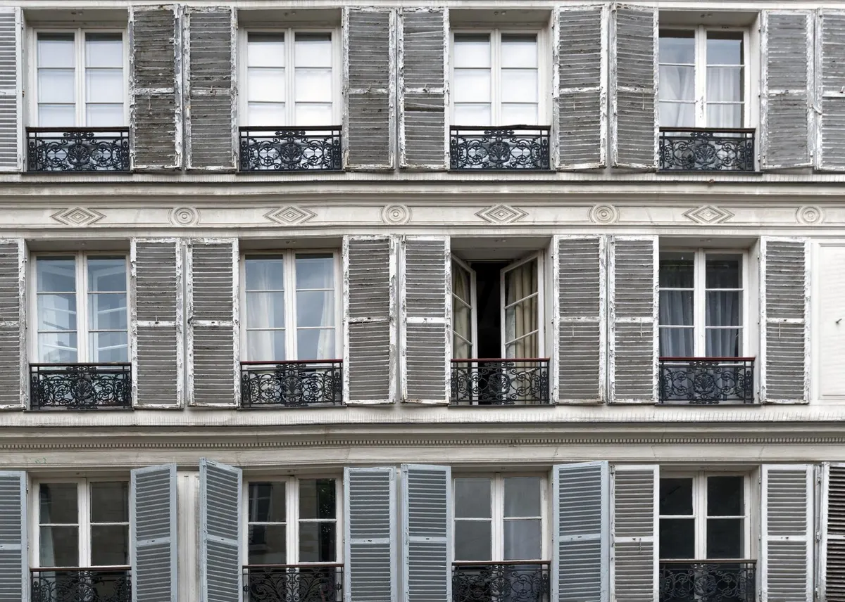 Façade d'immeuble ancien en pierre avec volets battants à persiennes et garde-corps en fer forgé