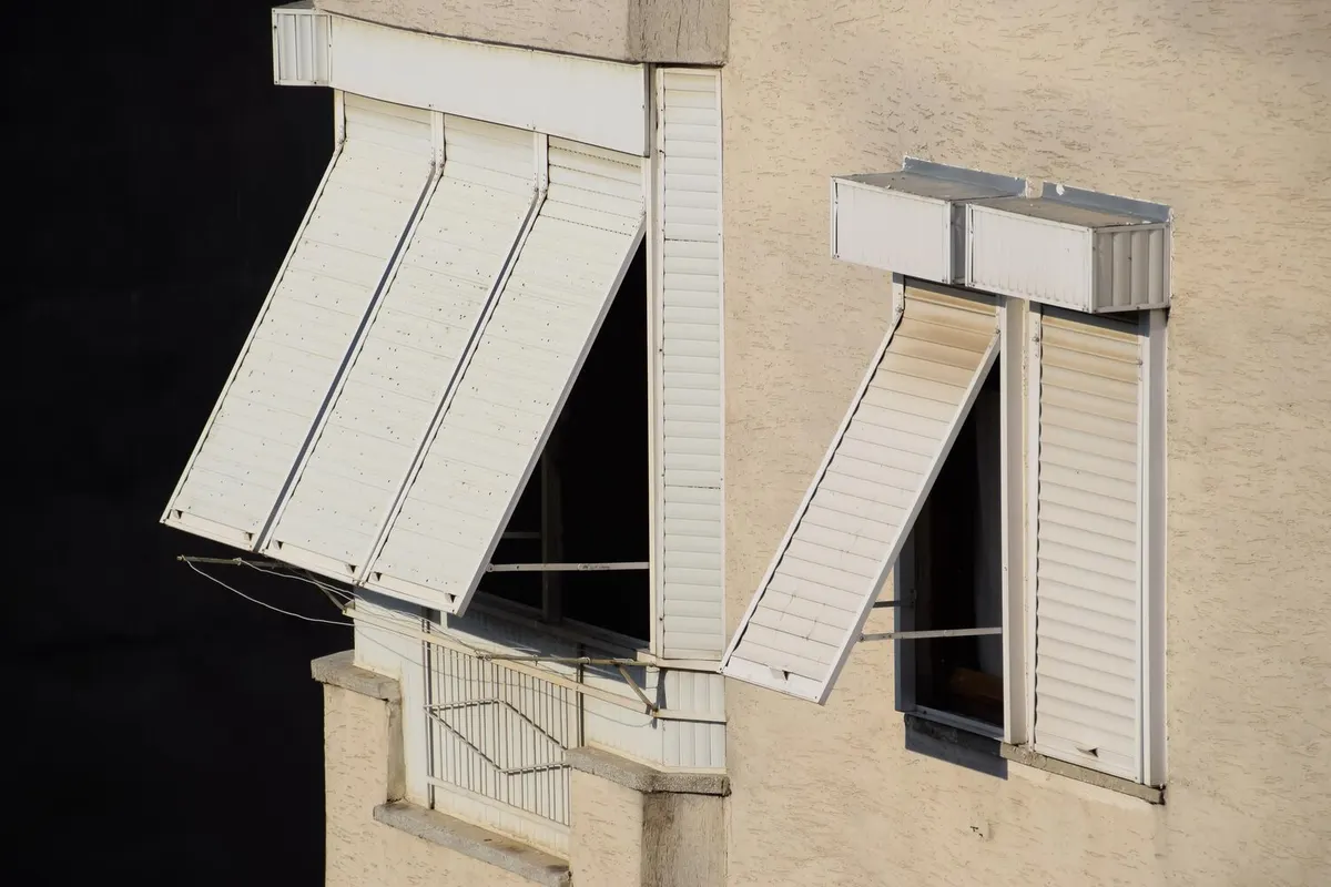 Volets roulants blancs à coffres extérieurs, certains tabliers projetés, sur la façade d'un immeuble collectif